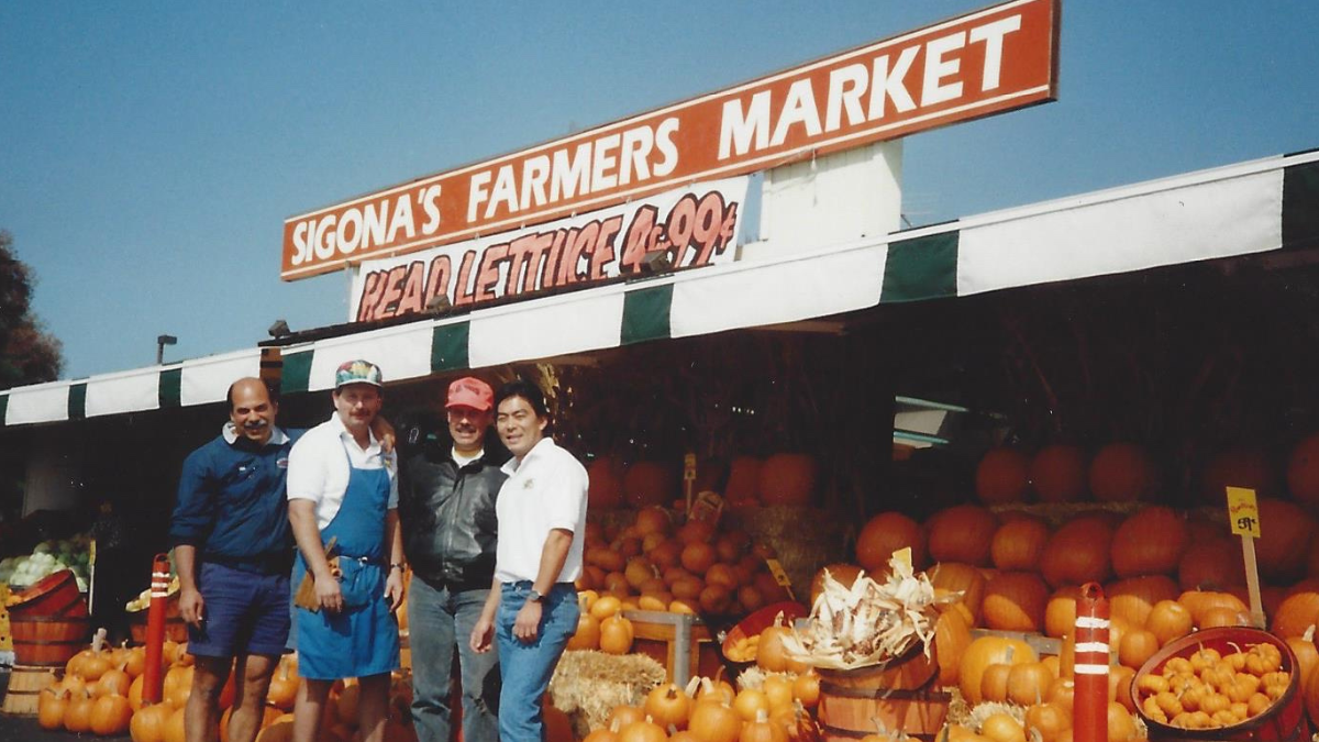 Four men stand in front of a storefront called "Sigona's Farmers Market"